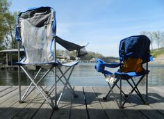 two folding chairs sitting on a wooden dock next to a body of water with trees in the background