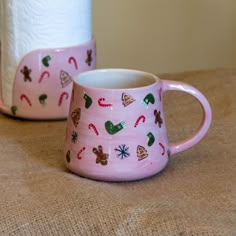 two pink mugs sitting next to each other on top of a brown cloth covered table