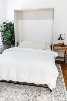 a white bed sitting on top of a wooden floor next to a green plant in a bedroom