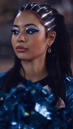 a woman with long hair and blue makeup looks at the camera while holding something in her hand