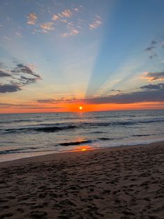 the sun is setting over the ocean with footprints in the sand