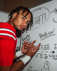 a man with dreadlocks standing in front of a whiteboard that has writing on it