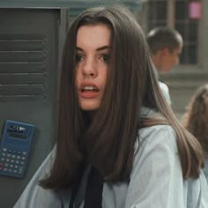 a woman with long hair standing next to a metal box and holding a calculator