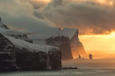 the sun is setting over an ice covered rock formation in the ocean with snow on it