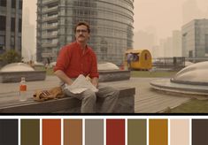 a man sitting on top of a wooden bench in front of tall buildings with lots of windows