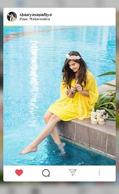 a woman sitting on the edge of a swimming pool holding a drink in her hand