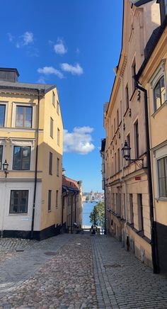 an empty cobblestone street with buildings on both sides and water in the distance