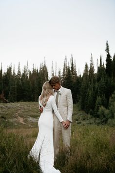 a bride and groom are standing in the tall grass with their arms around each other