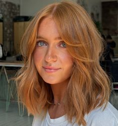 a woman with blonde hair and blue eyes looks into the camera while wearing a white t - shirt