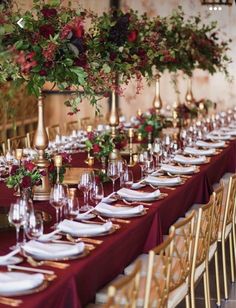 a long table is set with white plates and red napkins, gold candles and flowers