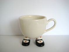 a white coffee cup with black shoes on the bottom and one foot sticking out from it