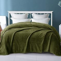 a bed with green bedspread and pillows in a blue walled room next to a white headboard