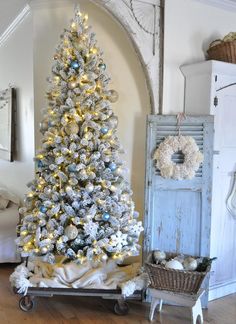 a white christmas tree with blue and silver ornaments on it in a living room next to an old door