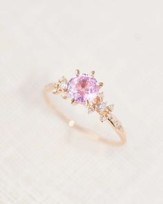 an engagement ring with a pink stone and three diamonds on the side, sitting on a white surface