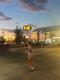 a woman standing in front of a gas station holding a cell phone