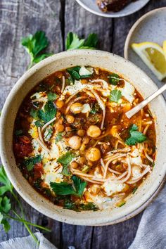 a bowl of soup with noodles, beans and parsley in it on a wooden table