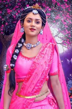 a woman in pink dress standing next to a tree with flowers on her head and chest