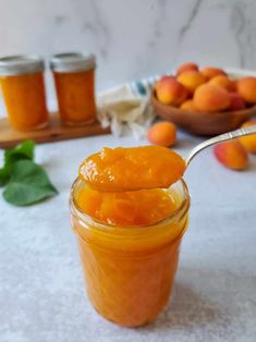 a spoon full of apricot jam sitting on top of a table next to some peaches