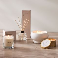 an assortment of candles, reeds and boxes on a wooden table with greenery