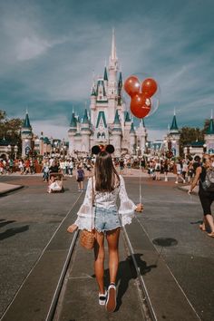 a woman is walking down the street in front of a castle with red heart balloons