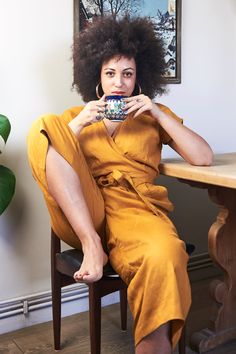 a woman sitting at a table with a cup in her hand and an afro hairdo