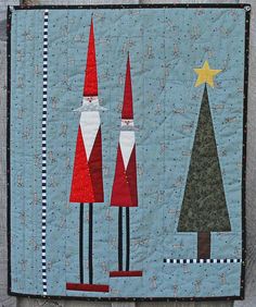 a quilted wall hanging with three gnomes and a star in the sky on it