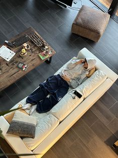 a man laying on top of a white couch in a living room next to a coffee table