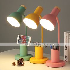 three different colored lamps sitting on top of a white table next to a book and phone