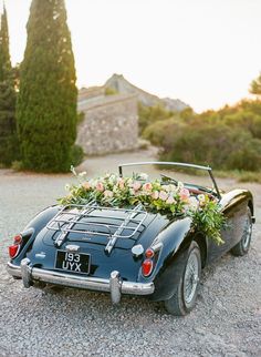 an old fashioned sports car decorated with flowers and greenery is parked on the gravel