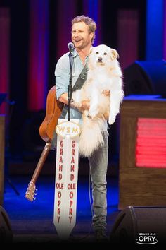 a man holding a white dog on top of a stage with a guitar in his hand