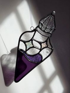 a stained glass sun catcher hanging from a hook on a wall with the shadow of a window behind it