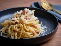 pasta with bacon and parmesan cheese in a black bowl on a wooden table