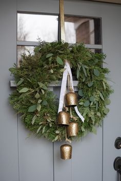 a wreath with bells hanging from it and greenery on the front door, next to a window