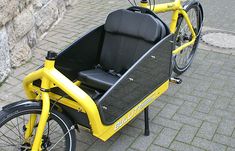 a yellow bike with a seat attached to the front and back, parked on a brick sidewalk