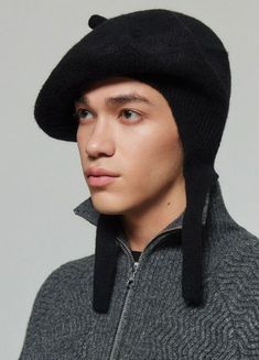 a young man wearing a black hat and grey sweater is looking at the camera with an intense look on his face