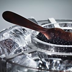 a wooden spoon sticking out of an ice bucket filled with water and blackberries in it