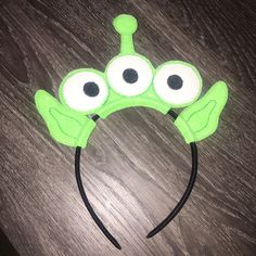 a green headband with googly eyes on top of a wooden table next to a pair of scissors