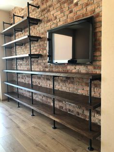 an entertainment center with shelves and a flat screen tv mounted on the wall, in front of a brick wall