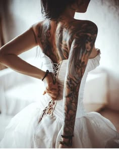 a woman with tattoos on her arms and arm is holding onto a white dress while sitting in front of a window