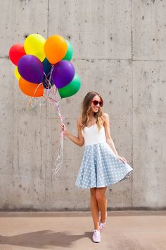 a young woman holding balloons in front of a concrete wall with sunglasses on her head