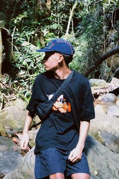 a young man sitting on top of a rock in the woods