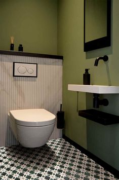 a white toilet sitting in a bathroom next to a sink and wall mounted faucet