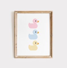 three rubber ducks in pastel colors on a white background framed in a wooden frame