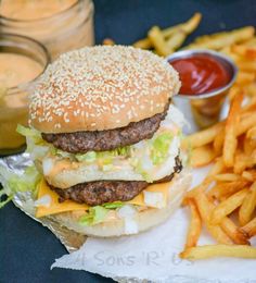 a hamburger with cheese and lettuce next to french fries on wax paper in front of some ketchup