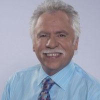 an older man wearing a blue shirt, tie and dress shirt smiling at the camera