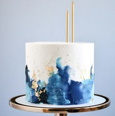 a white and blue cake with gold sprinkles sitting on a metal stand