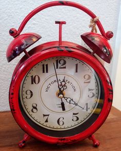 an old red alarm clock sitting on top of a wooden table