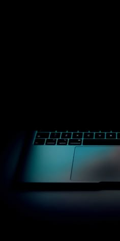 a laptop computer sitting on top of a desk in the dark with its keyboard lit up