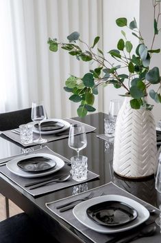 a table set with place settings, plates and silverware in front of a white vase