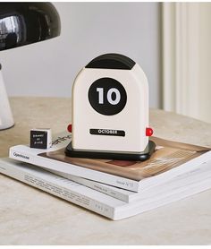 a white and black clock sitting on top of some books next to a desk lamp